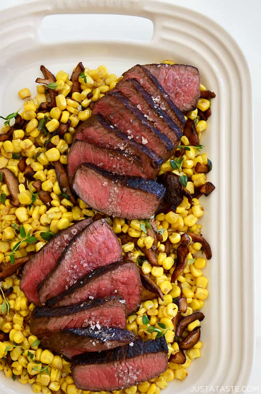 A white platter with corn, mushrooms and sliced steak