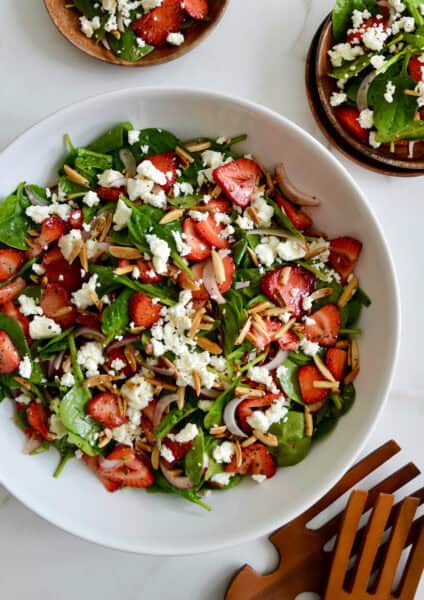 A white serving bowl containing Spinach Strawberry Salad with Poppy Seed Dressing.