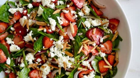 A white serving bowl containing Spinach Strawberry Salad with Poppy Seed Dressing.