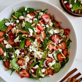 A top down view of a white bowl containing Spinach Strawberry Salad with Poppy Seed Dressing