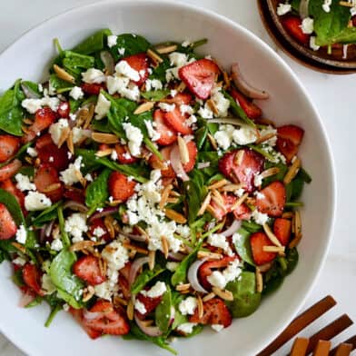 A top down view of a white bowl containing Spinach Strawberry Salad with Poppy Seed Dressing