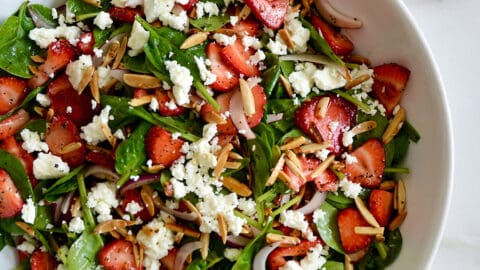 A top down view of a white bowl containing Spinach Strawberry Salad with Poppy Seed Dressing