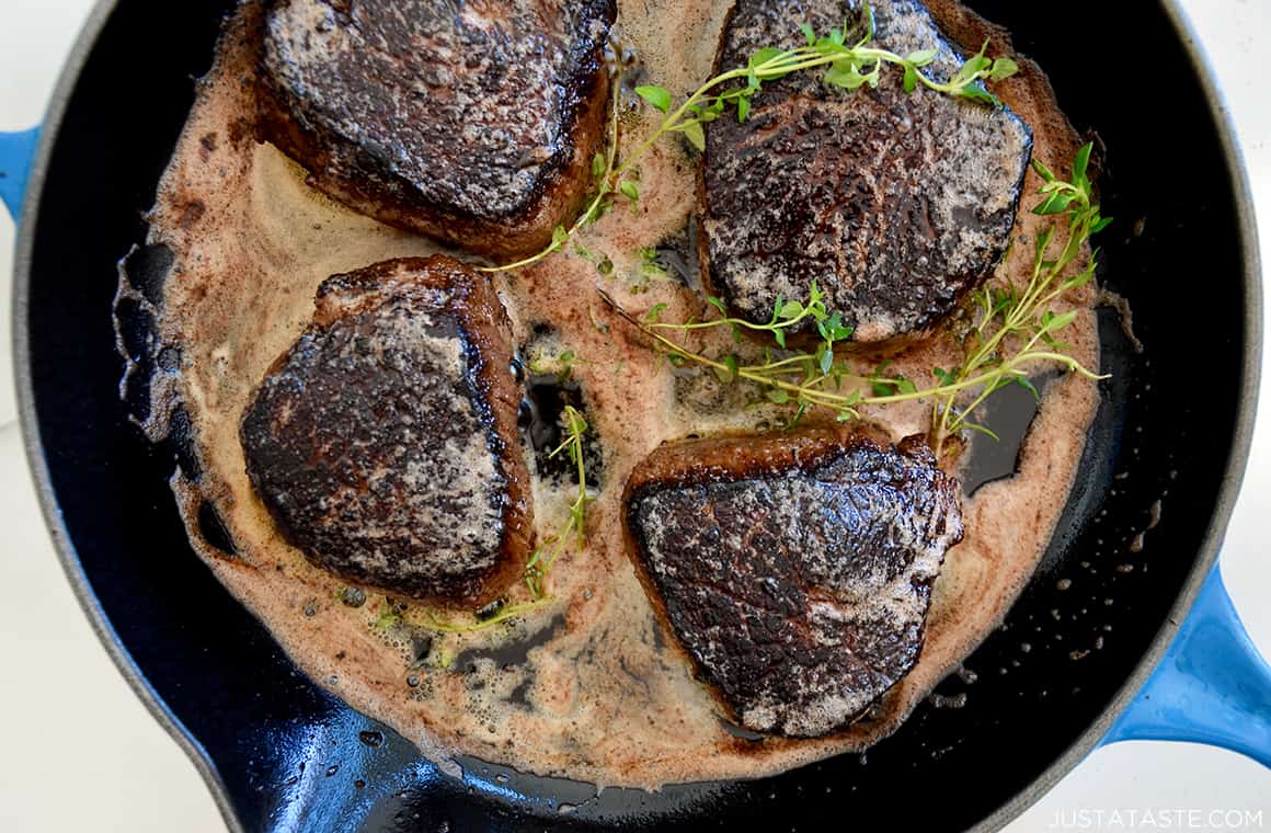 A blue skillet with steaks, butter and thyme