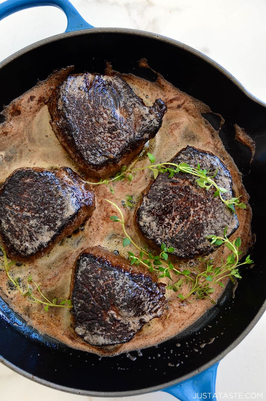 A blue skillet containing steaks with thyme and butter