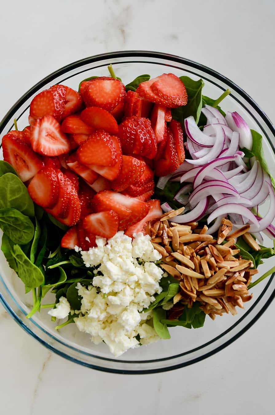 A glass bowl containing spinach, strawberries, onions, nuts and feta cheese