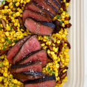 Top-down view of sliced steak sprinkled with sea salt over a bed of corn and mushrooms.