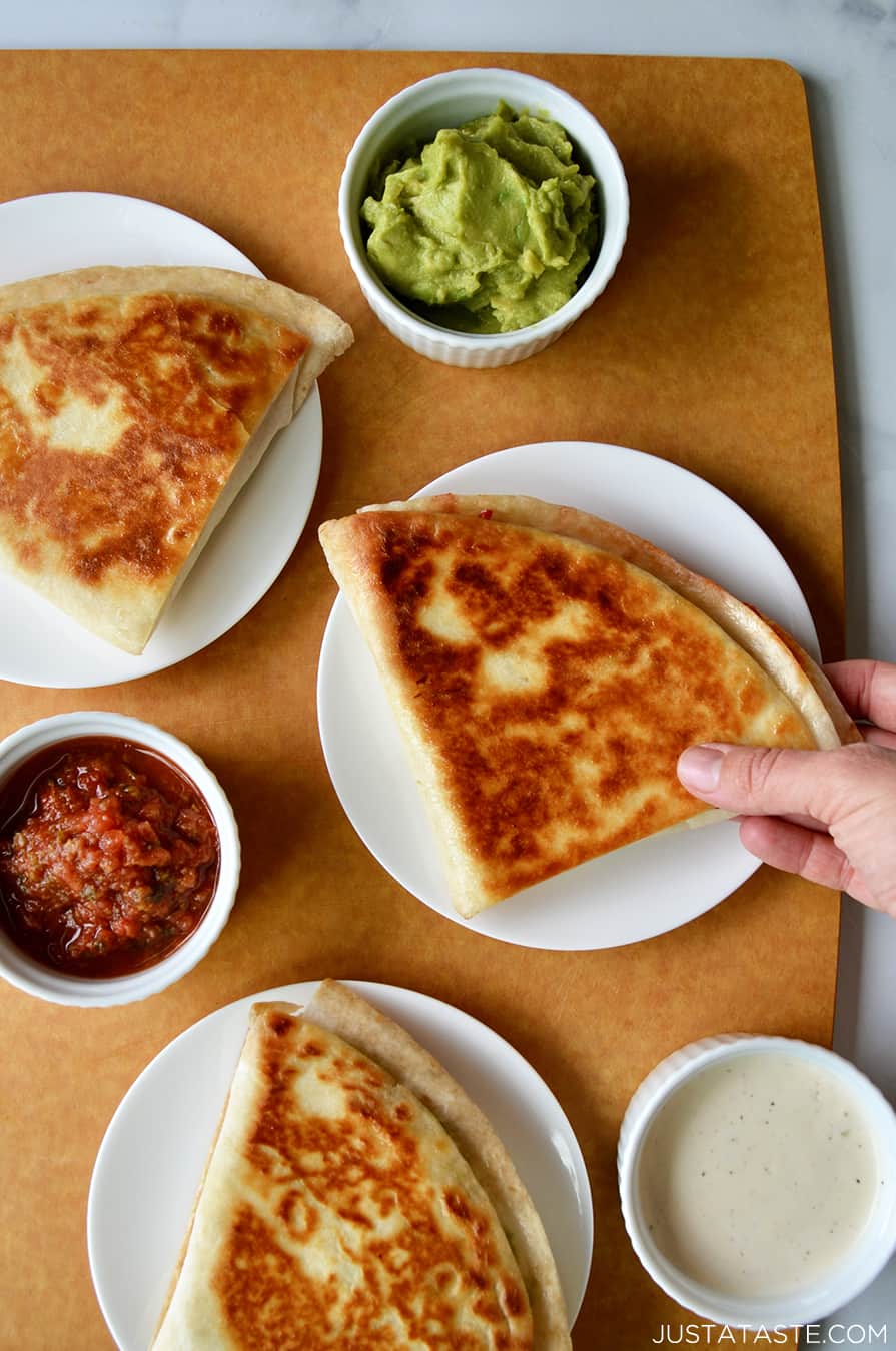 Three tortillas using the Tortilla Wrap Hack method on plates next to ramekins filled with guacamole, salsa and ranch dressing