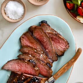 Sliced tri-tip on a blue serving platter with salt and pepper