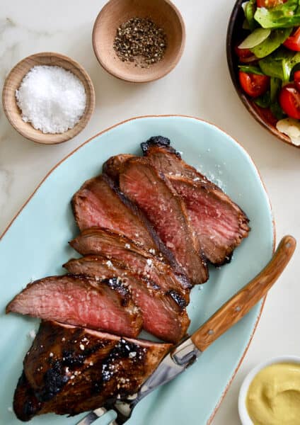 Sliced tri-tip on a blue serving platter with salt and pepper