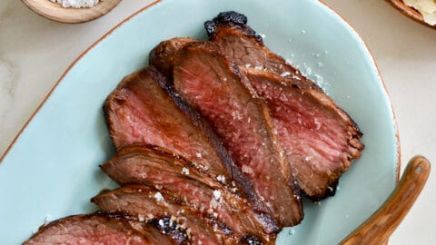 Sliced tri-tip on a blue serving platter with salt and pepper