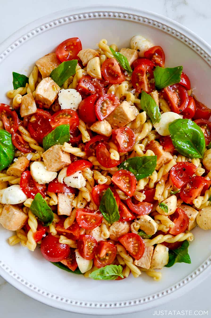 A large white bowl containing pasta salad with tomatoes and basil