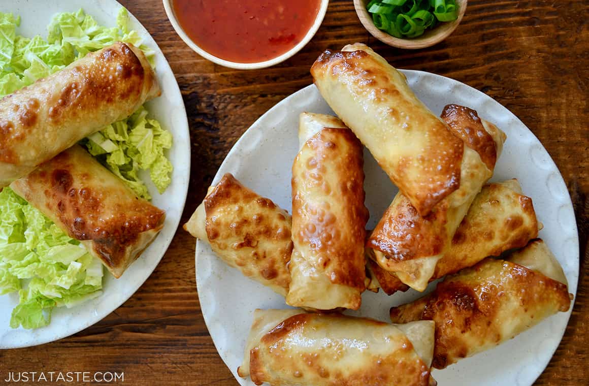 Air Fryer Egg Rolls piled on a plate next to a small bowl containing sweet chili sauce