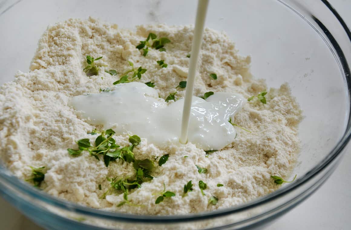 Buttermilk being poured into biscuit dough with thyme