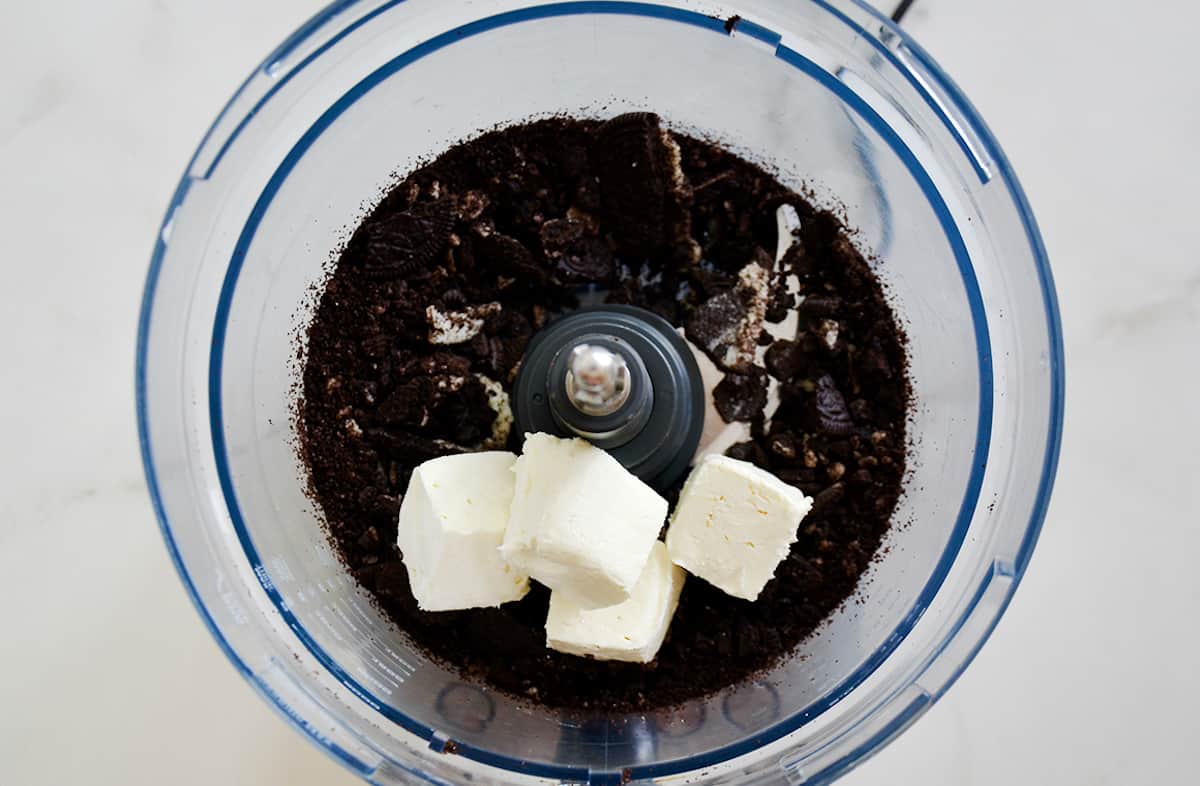 Crushed Oreos and cream cheese in the bowl of a food processor.