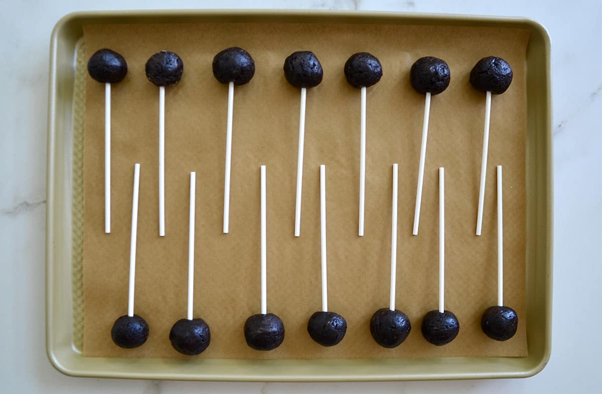 Chocolate cookie pops with popsicle sticks on a parchment paper-lined baking sheet.