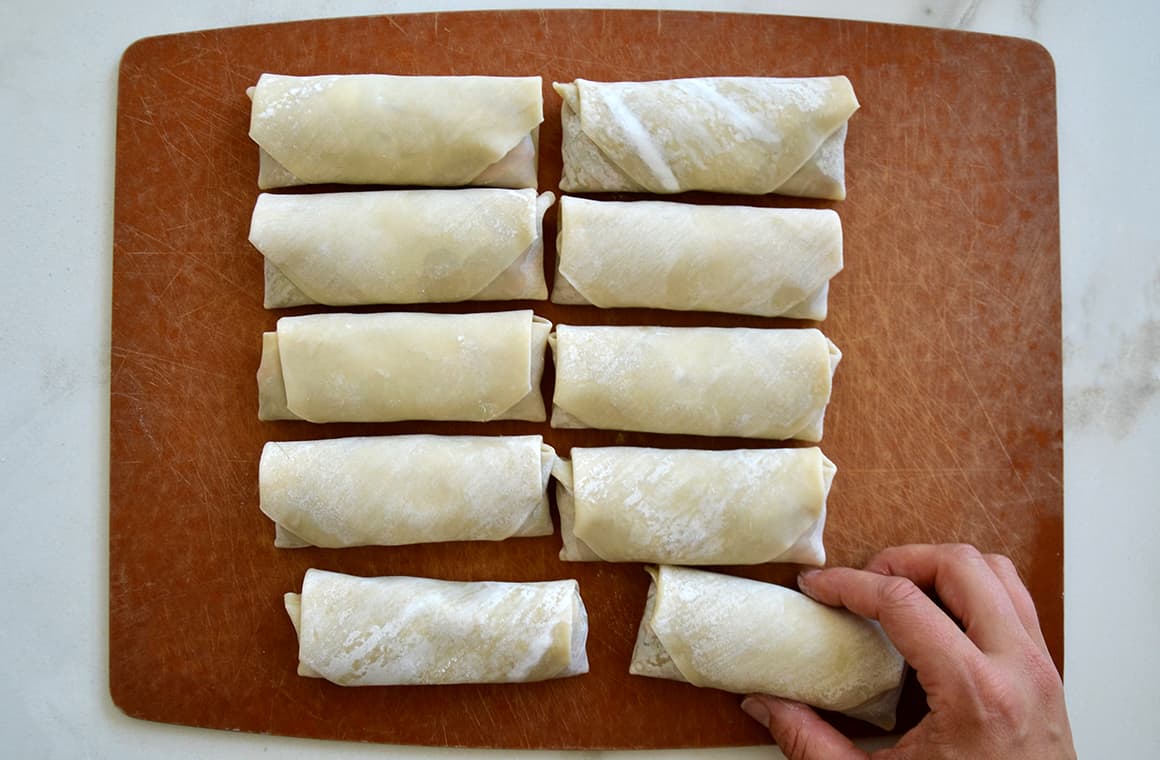 Two rows of formed egg rolls with a hand reaching for one of them