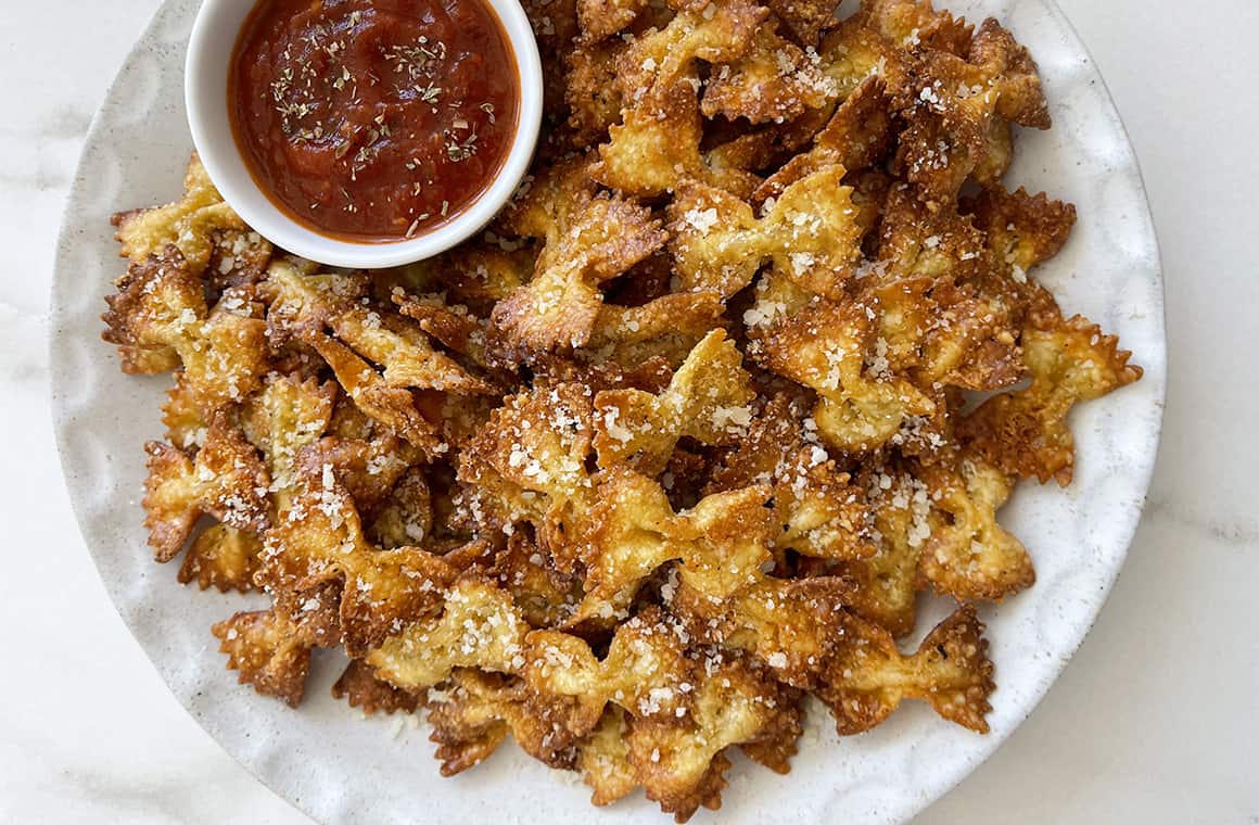 A white plate containing pasta chips topped with grated Parmesan cheese