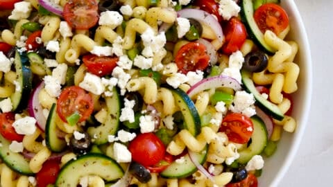 Greek pasta salad with feta, tomatoes, cucumbers and olives in a large serving bowl.