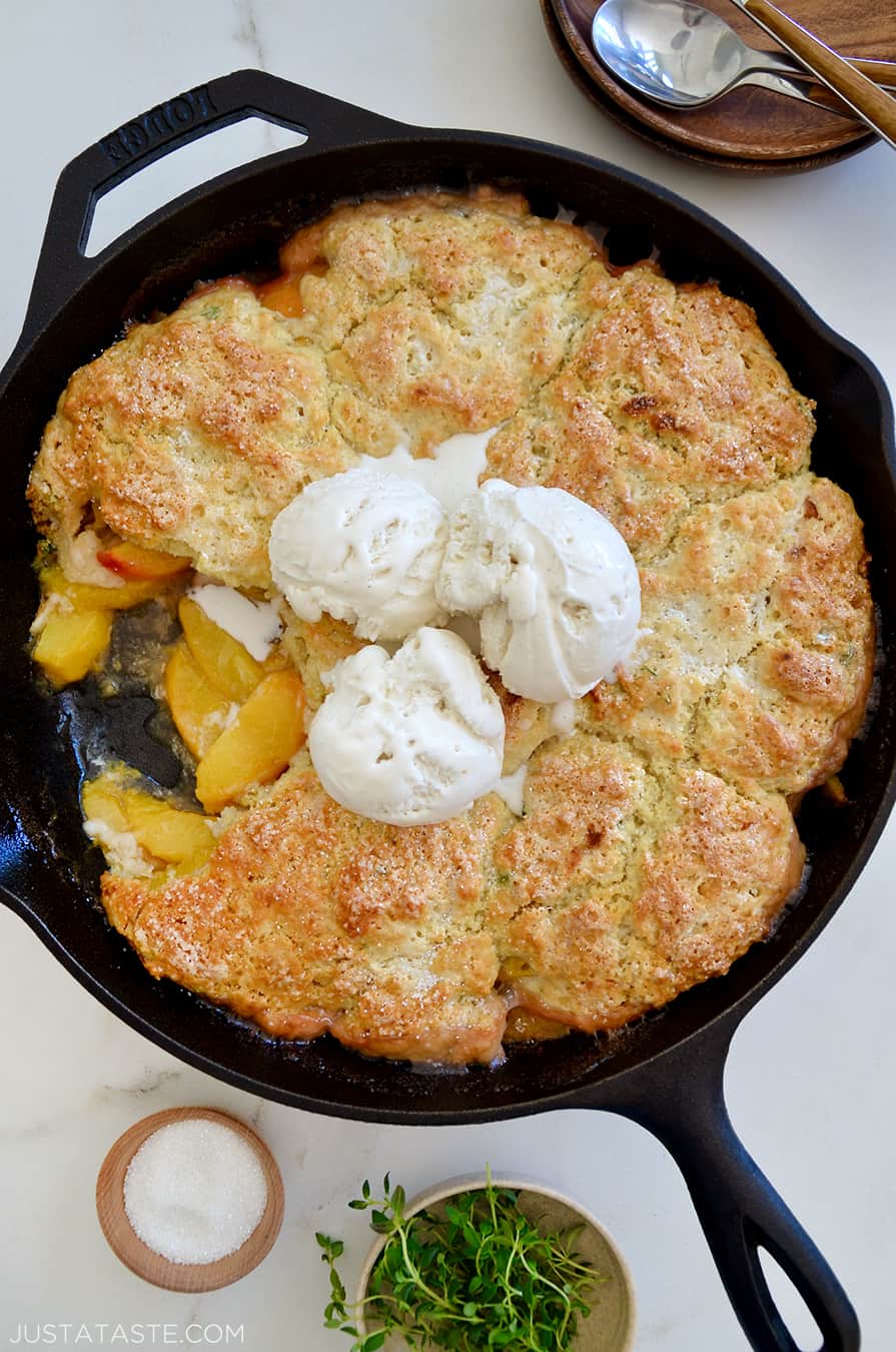 A cast-iron skillet containing peach cobbler with ice cream on top