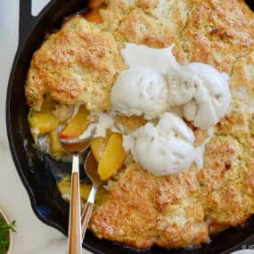 Peach cobbler in a cast-iron skillet with melting ice cream on top