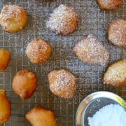 Apple Fritters dusted with powdered sugar on a wire cooling rack over a baking sheet.