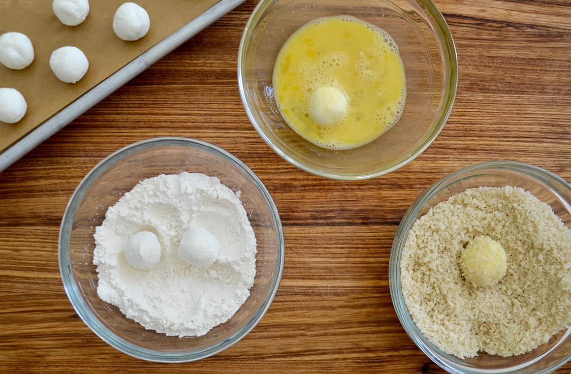 Three bowls containing flour, eggs and breadcrumbs with goat cheese balls