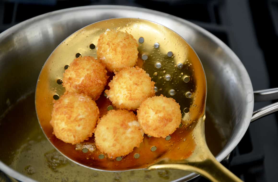 A spoon filled with goat cheese balls after they've been fried