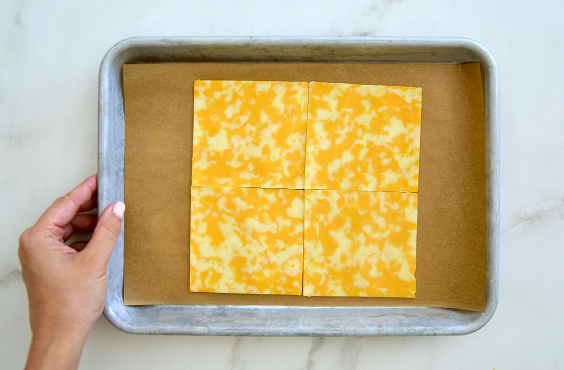 Four slices of cheese arranged on parchment paper on a baking sheet