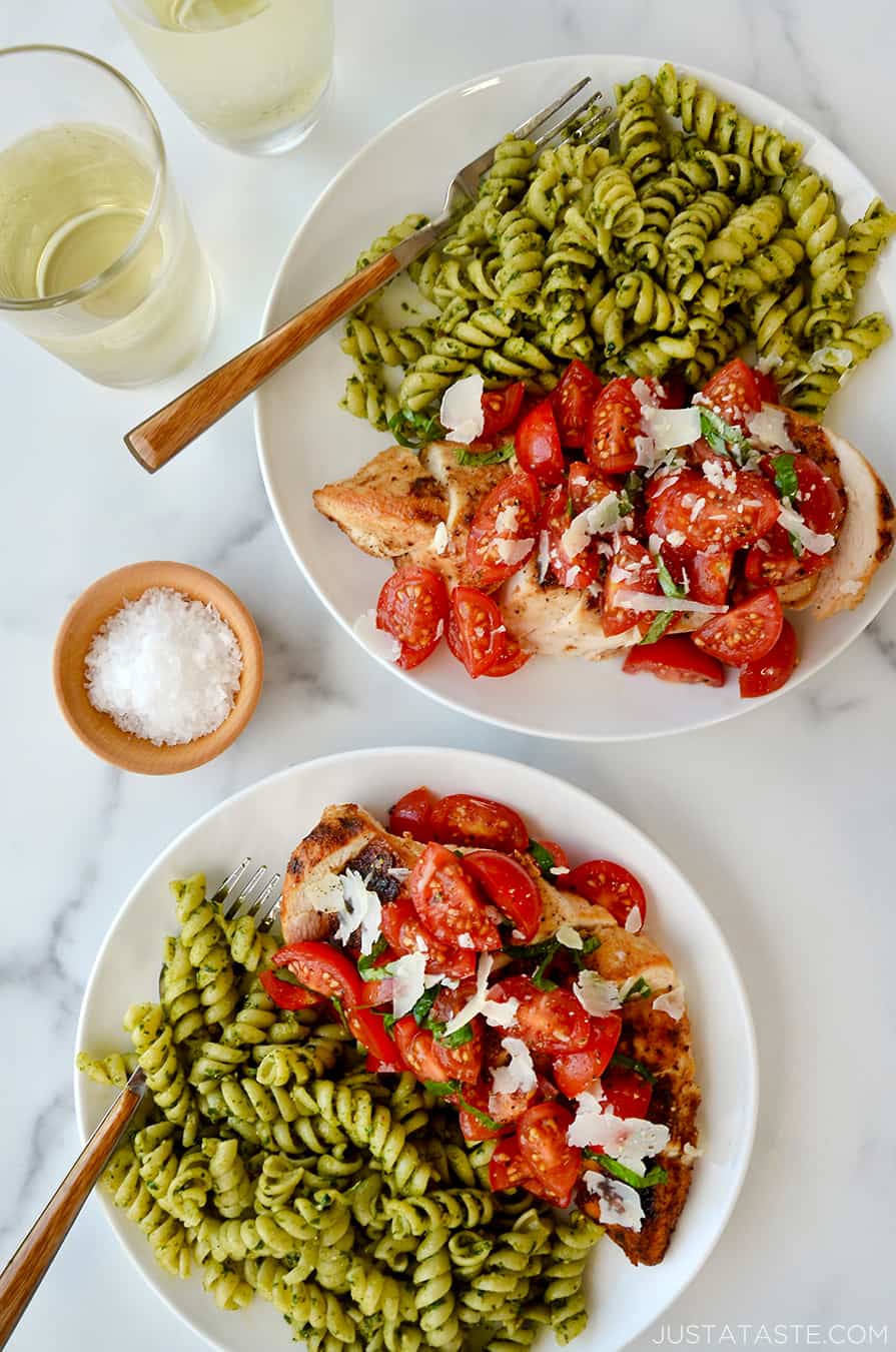 White plates containing bruschetta chicken and rotini pesto pasta