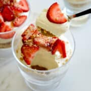 A spoon with no-bake cheesecake and a strawberry over a parfait glass filled with creamy cheesecake and fresh strawberries.