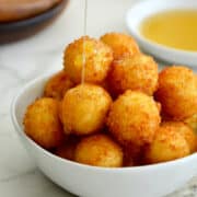 Fried Goat Cheese Balls piled high in a white bowl being drizzled with honey.