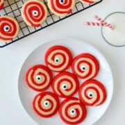 Monster Eye Halloween Cookies on a white plate next to a glass of milk and wire cooling rack containing more cookies.