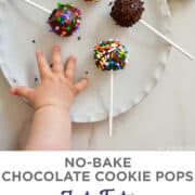 A child's hand reaching for No-Bake Chocolate Cookie Pops decorated with rainbow sprinkles on a white plate.