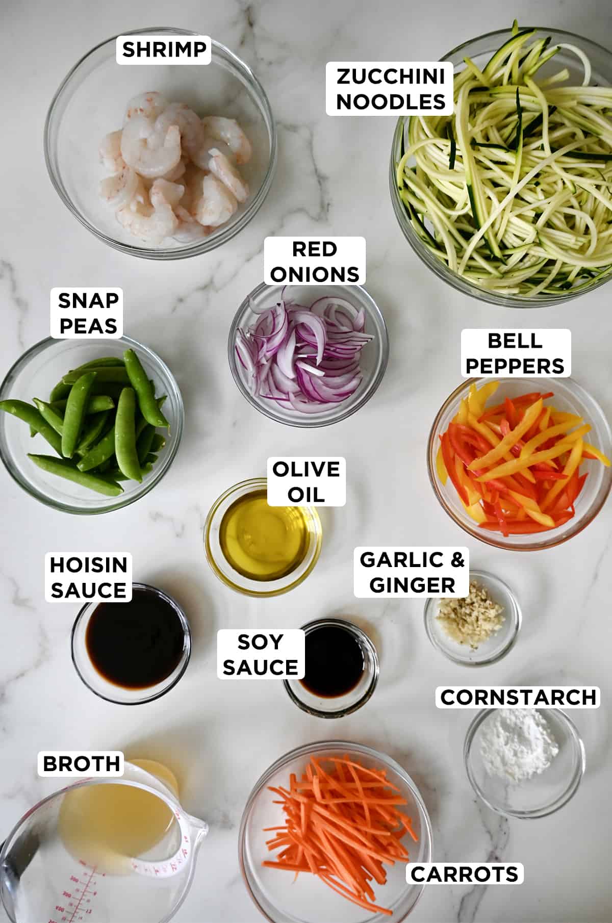 Small glass bowls containing ingredients for stir fry with zucchini noodles and shrimp.