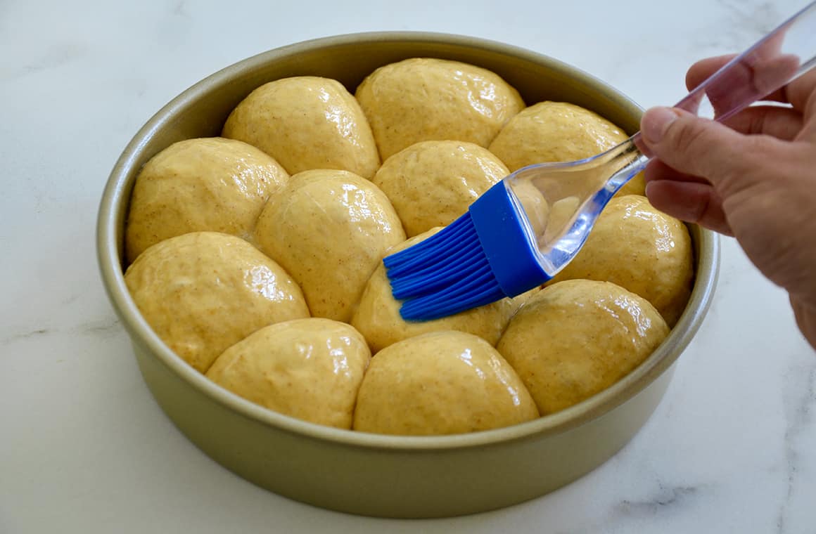 Pumpkin dinner rolls getting brushed with butter