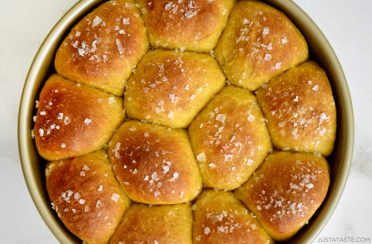 Buttery pumpkin bread rolls topped with large-flake sea salt in a round baking dish.
