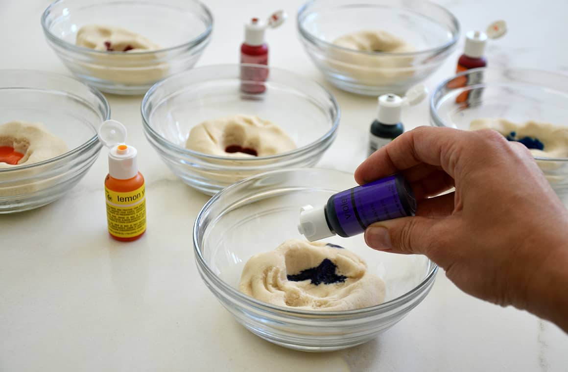 Food coloring being squeezed into a glass bowl with playdough