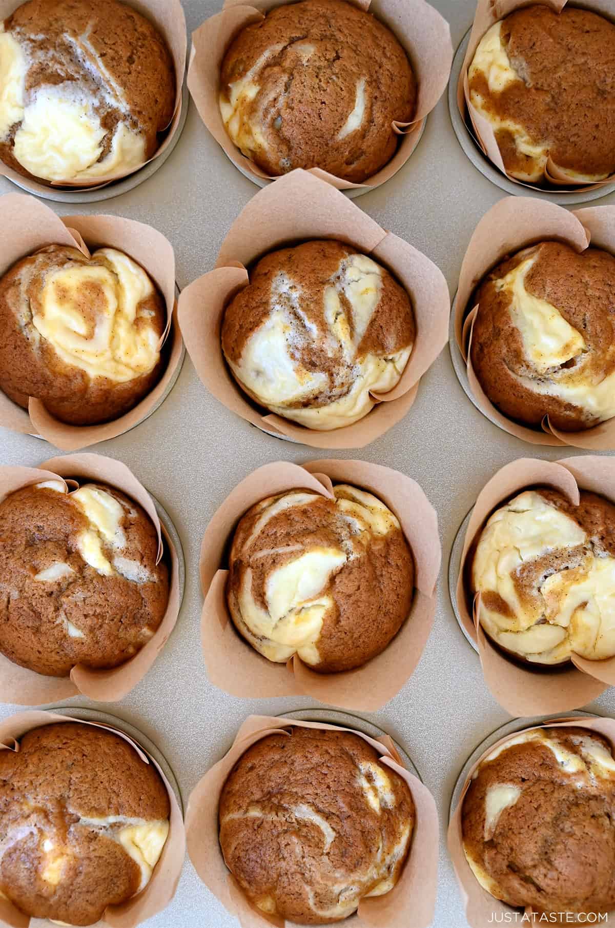 Freshly baked pumpkin muffins with swirls of creamy cheesecake, cooling in a muffin tin.