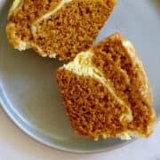 A pumpkin muffin with a ribbon of cream cheese cut in half on a plate.
