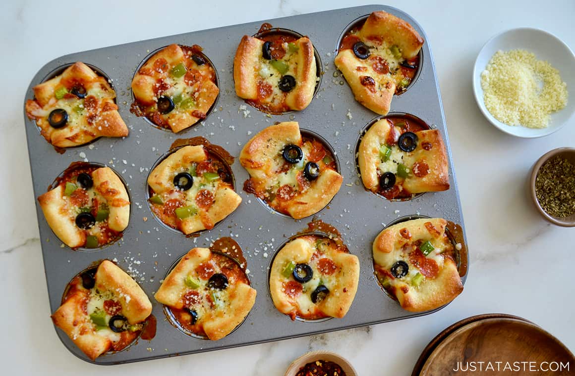 A top-down view of a muffin pan containing mini Easy Cheesy Pizza Cups with black olives and green peppers