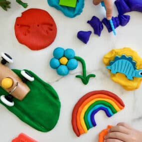A top-down view of a rainbow of homemade playdough colors with toys