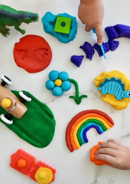 A top-down view of a rainbow of homemade playdough colors with toys