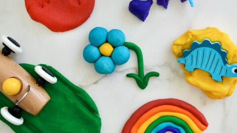 A top-down view of a rainbow of homemade playdough colors with toys