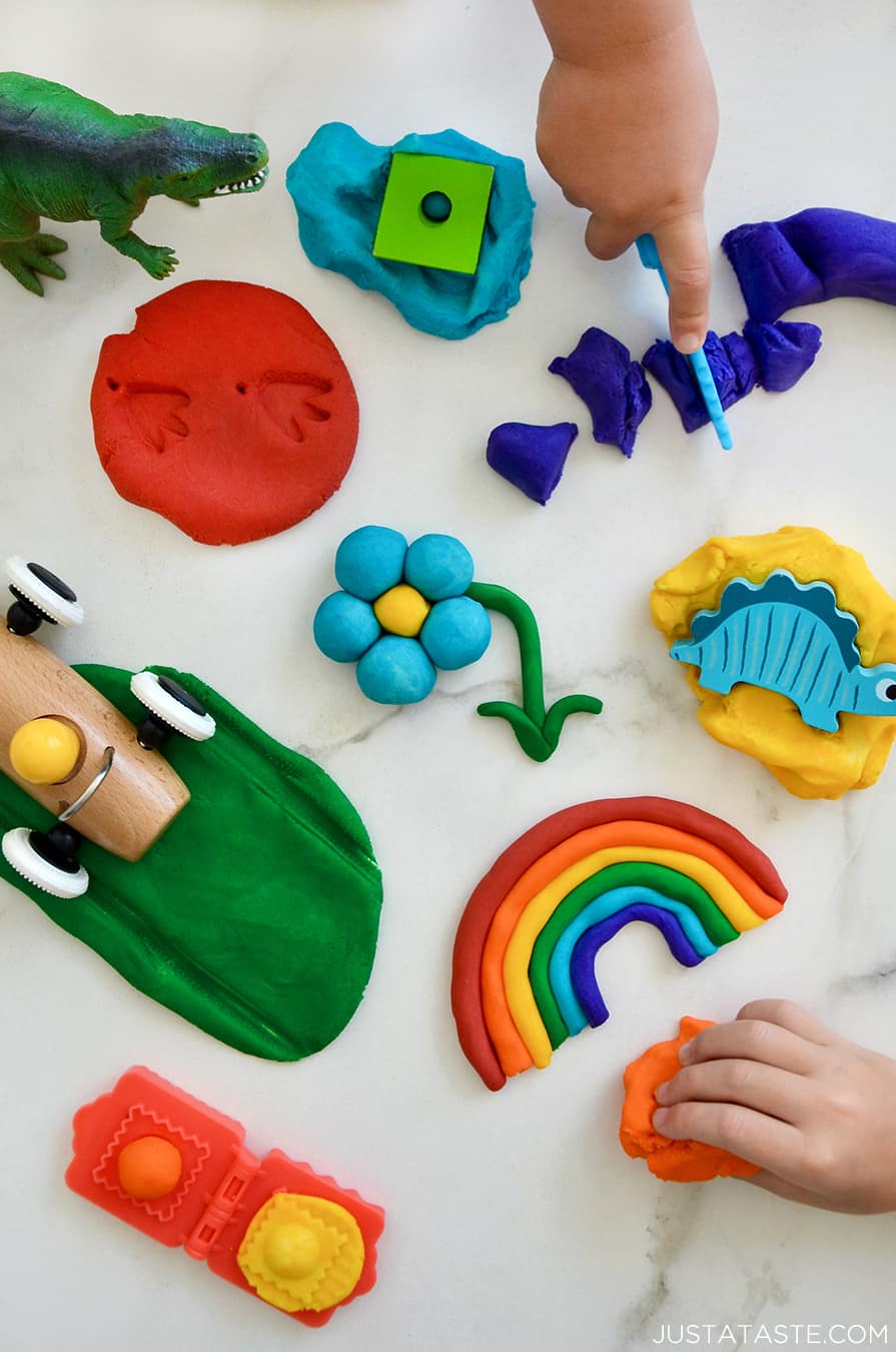 A top-down view of a rainbow of homemade playdough colors with toys