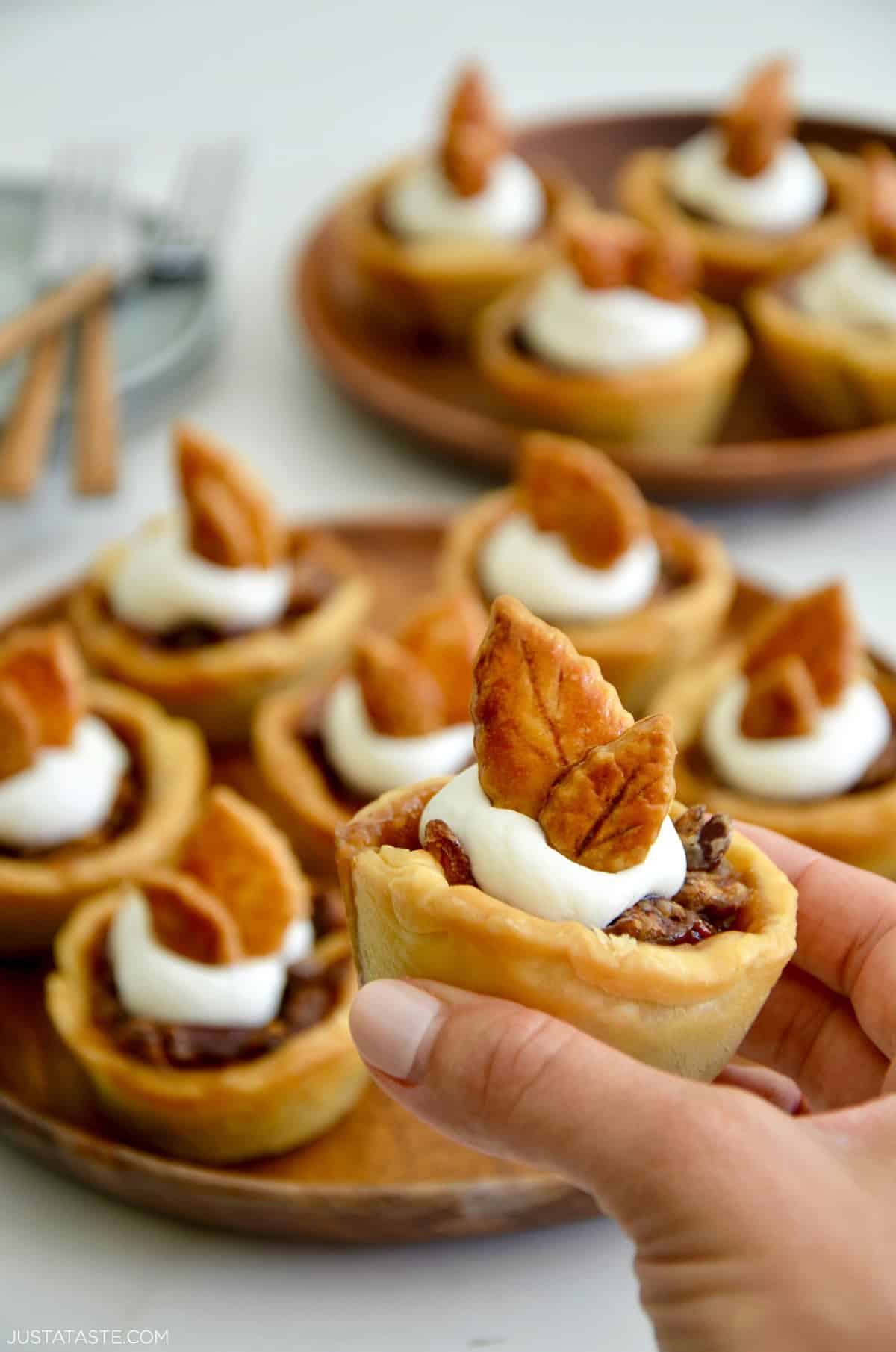 A hand holding a mini pecan pie garnished with whipped cream.