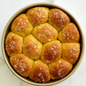 A top down view of pumpkin dinner rolls in a gold baking pan