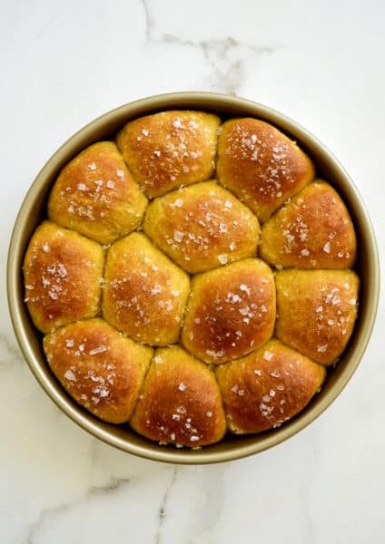 A top down view of pumpkin dinner rolls in a gold baking pan