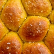 A close-up view of golden-brown Homemade Pumpkin Dinner Rolls topped with large-flake sea salt.