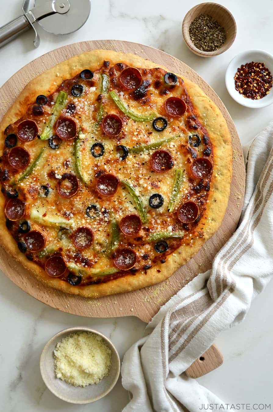 A top-down view of pizza on a wood board with bowls of cheese and seasonings