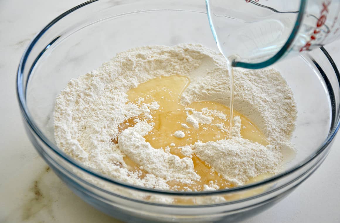 A glass bowl containing flour and salt with oil being streamed in
